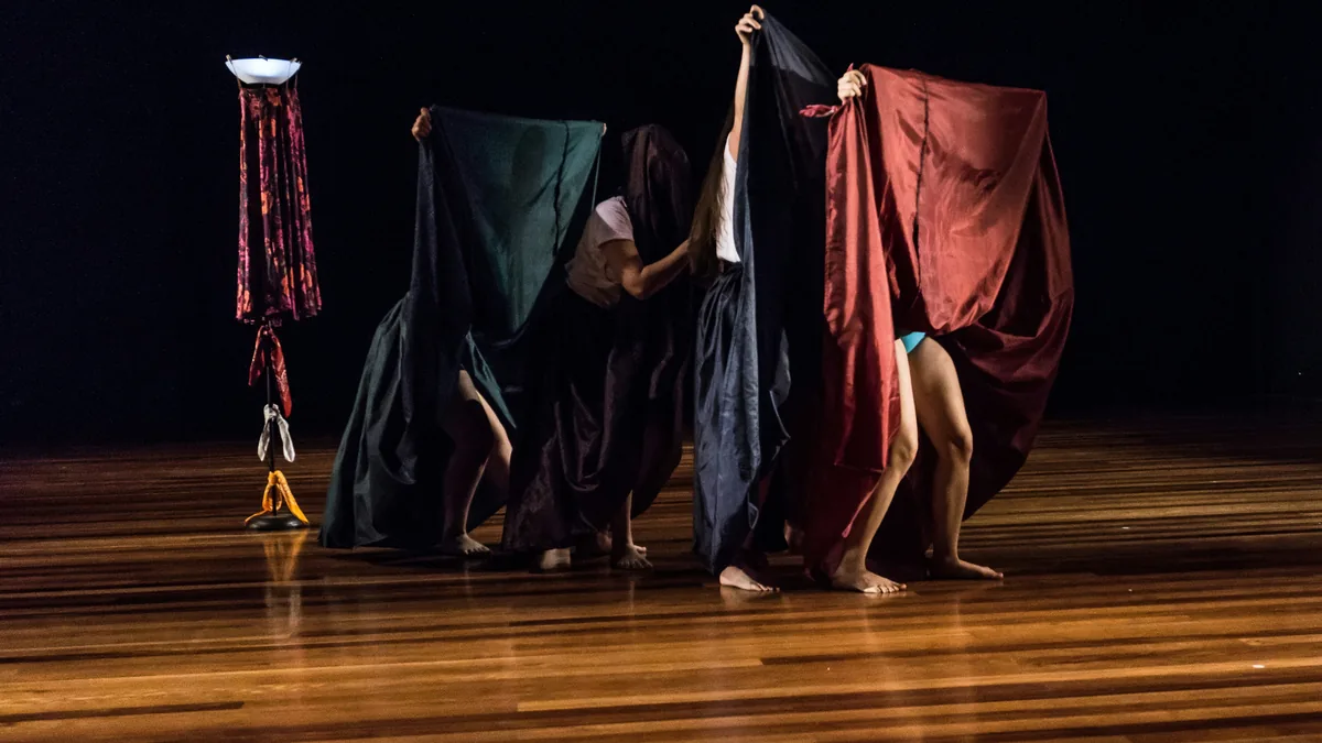 Performers using draped fabrics on a stage during an expressive movement piece.