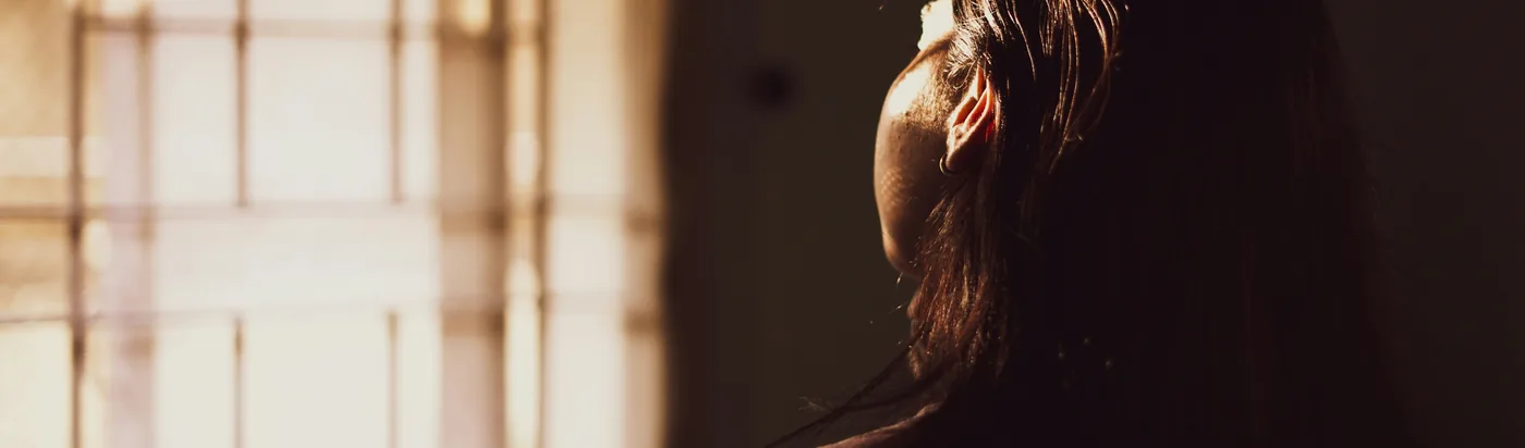An adult in side profile near a window, head slightly tilted, in a moment of reflection.