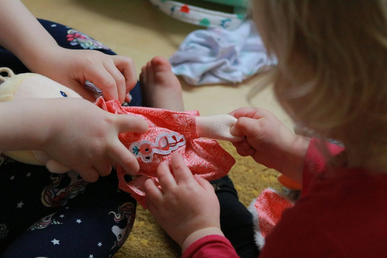 Children's hands engaged in dressing a soft doll during play.