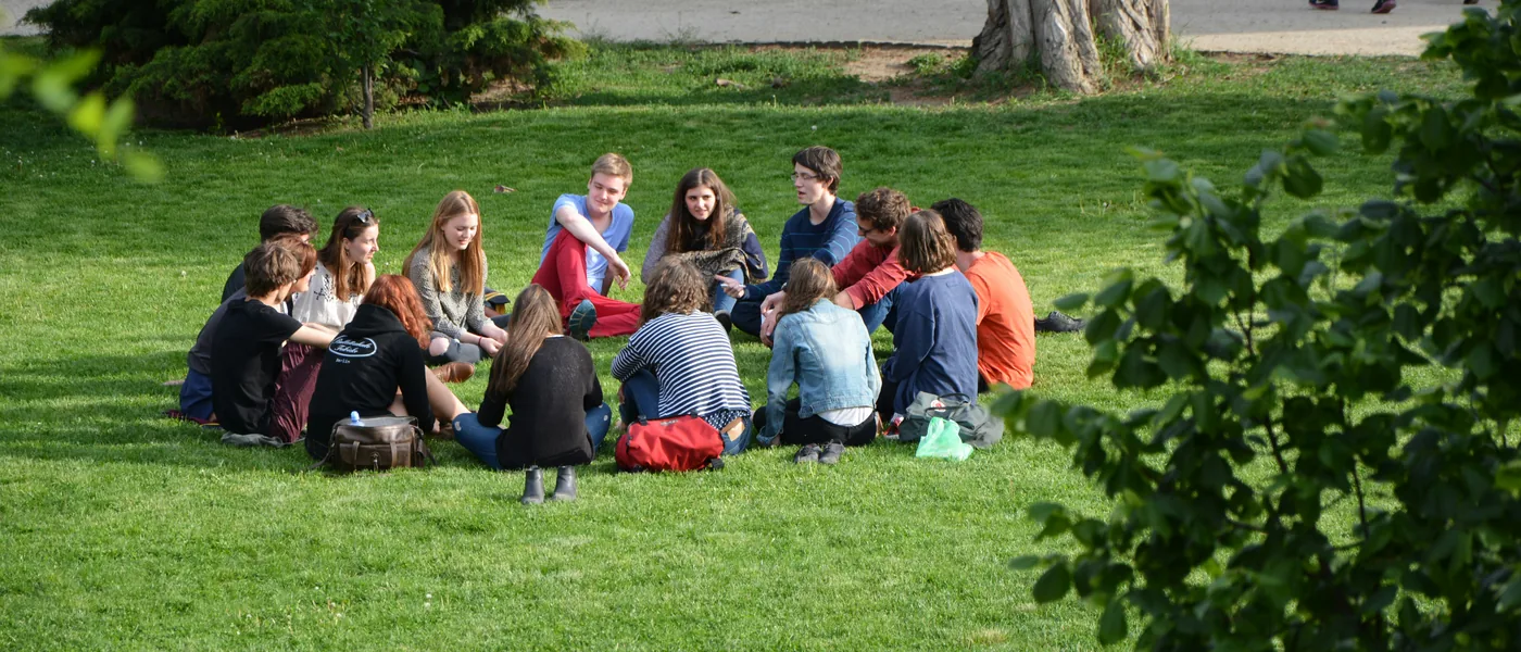 A group seated together in a circle on the grass under sunlight, embodied connection in shared space.
