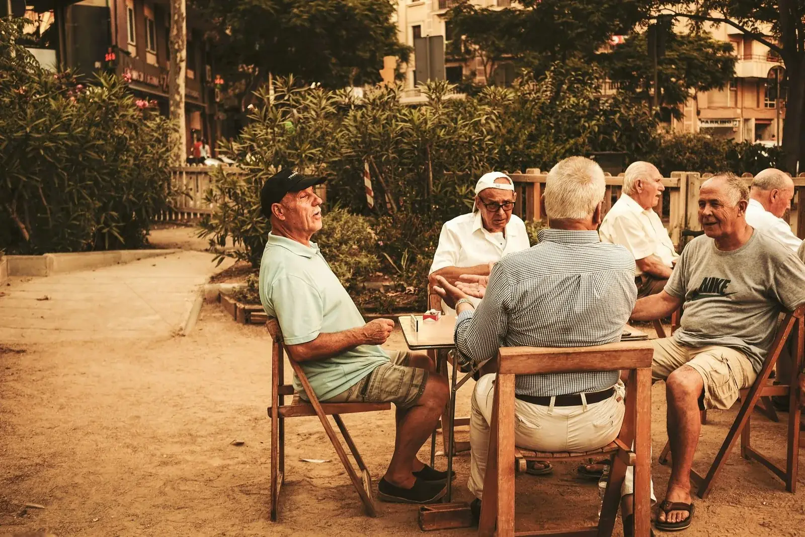 Older adults gathered around an outdoor table, talking in warm light.