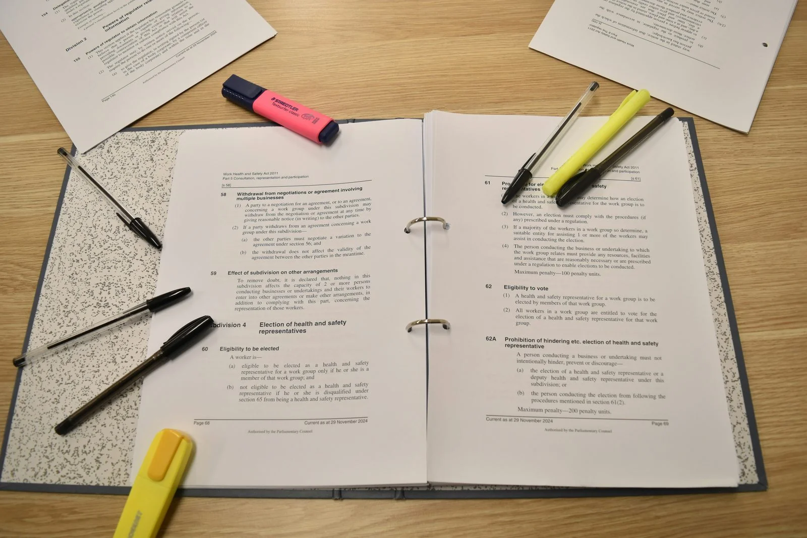 Open binder of research pages with highlighters and pens on a desk.