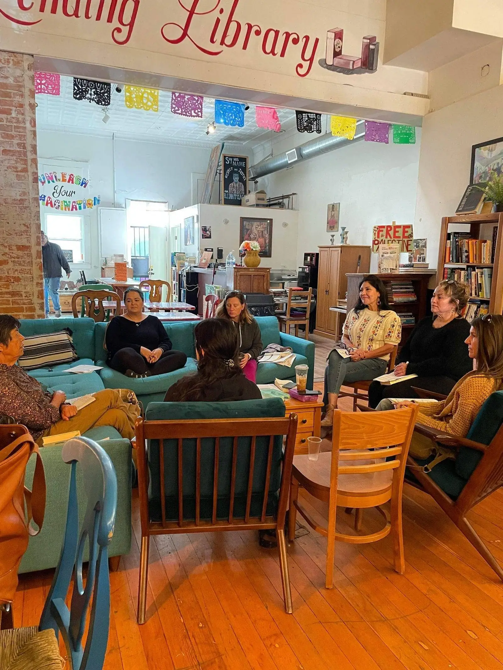 Group seated in a circle in a community space with bookshelves and creative decor.
