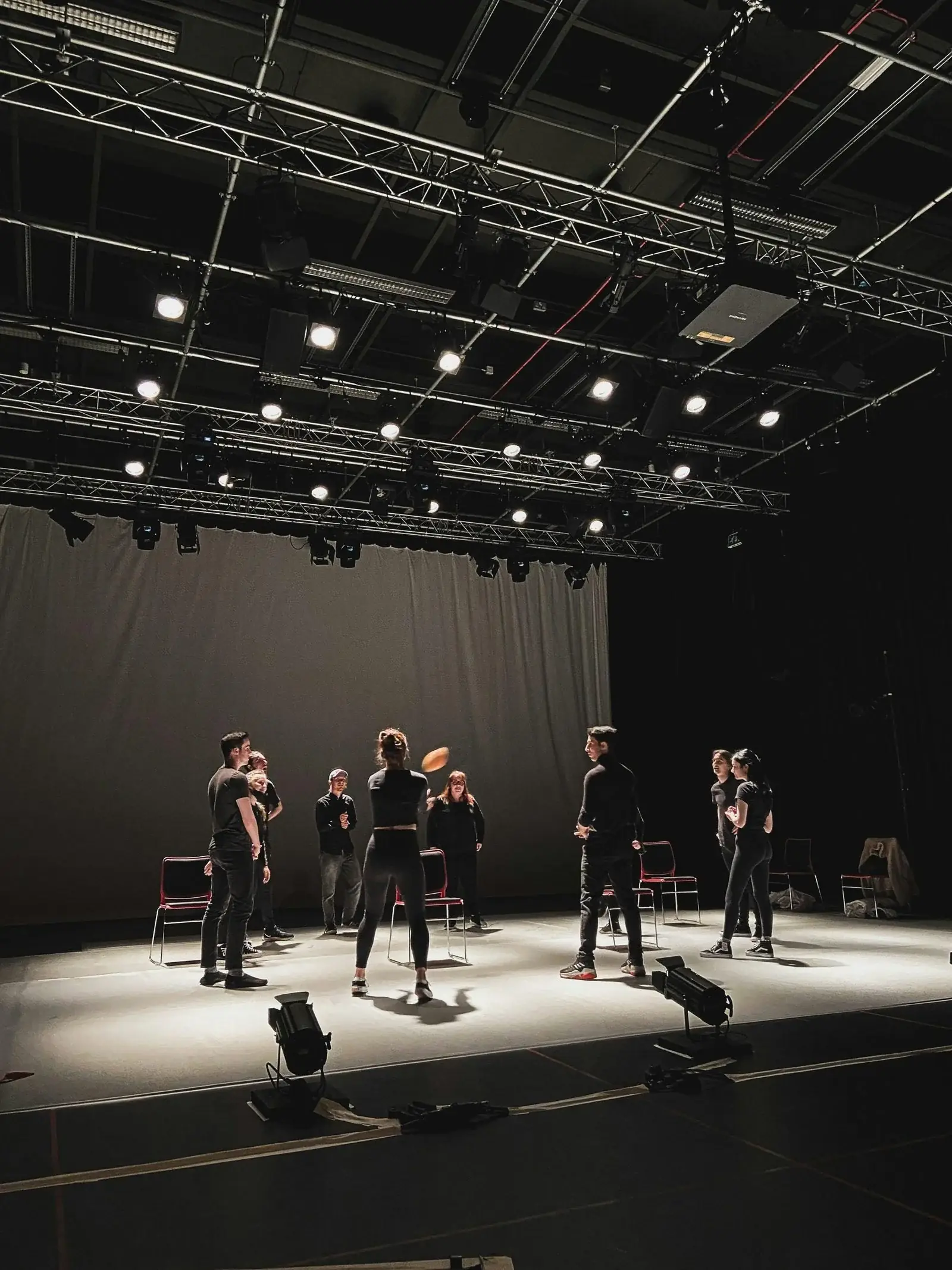 Black-box theatre studio with performers rehearsing under stage lights.